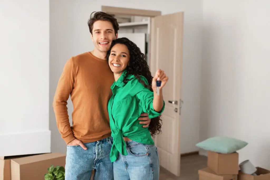 Smiling couple holding up their new house keys in the doorway of their home