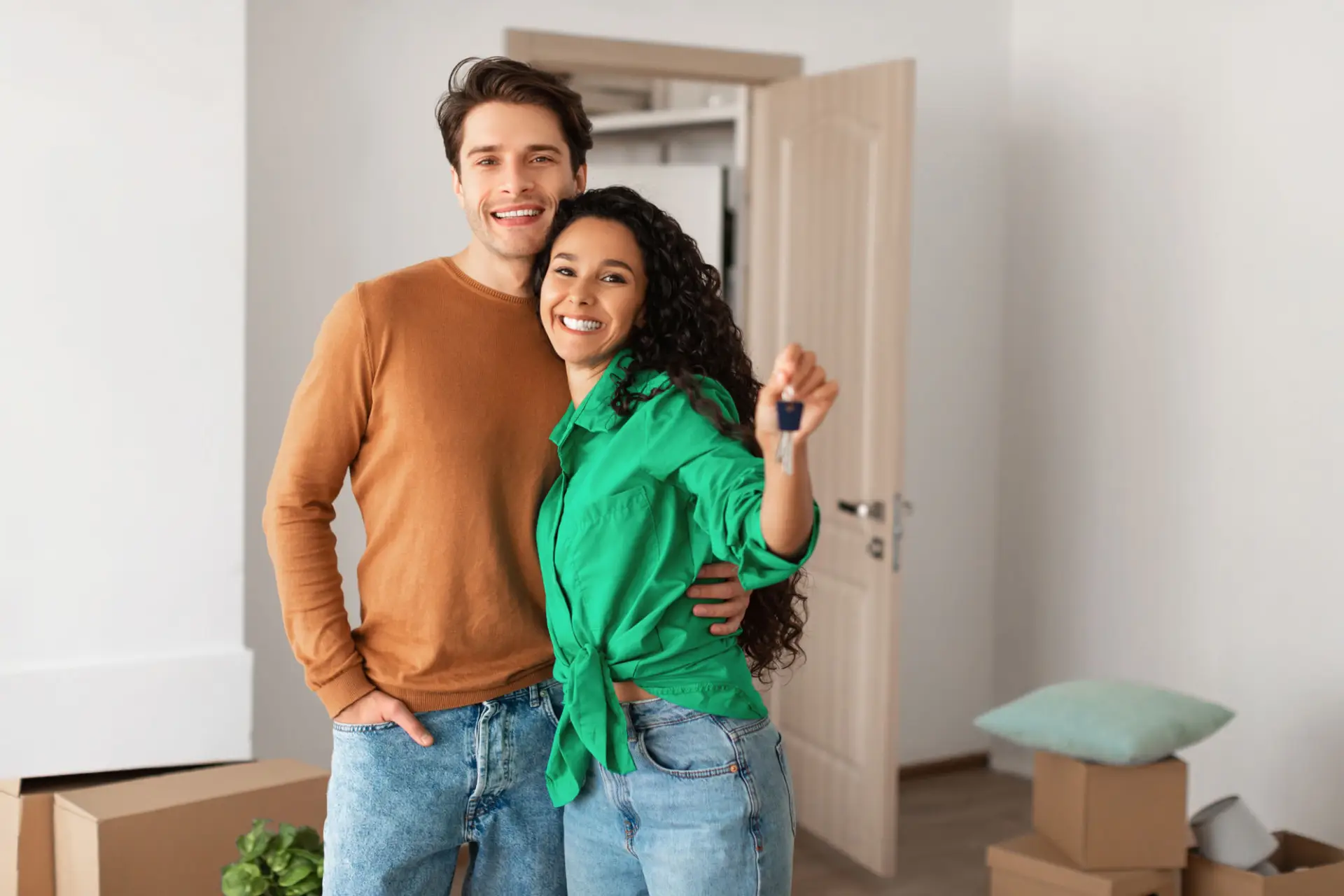 Smiling couple holding up their new house keys in the doorway of their home