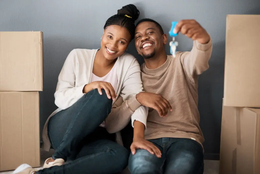 Young couple holding up the keys to their first home among moving boxes